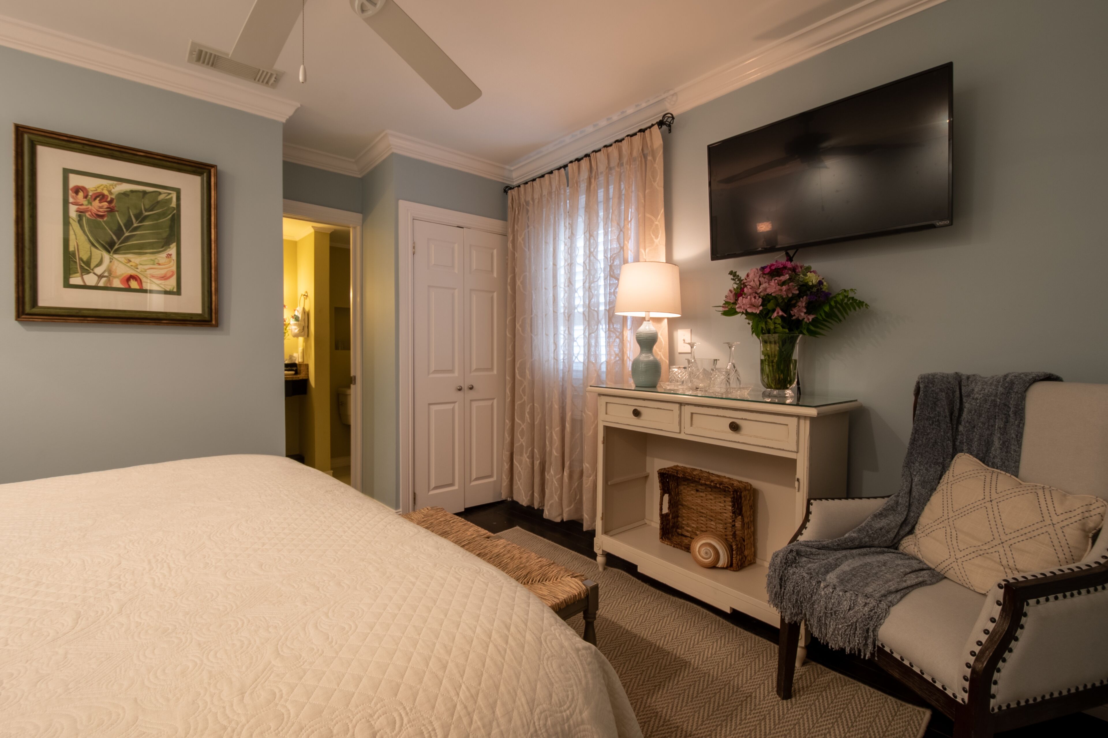 Une chambre à coucher avec un grand lit, une table de chevet avec une lampe, une chaise et un téléviseur fixé au mur.