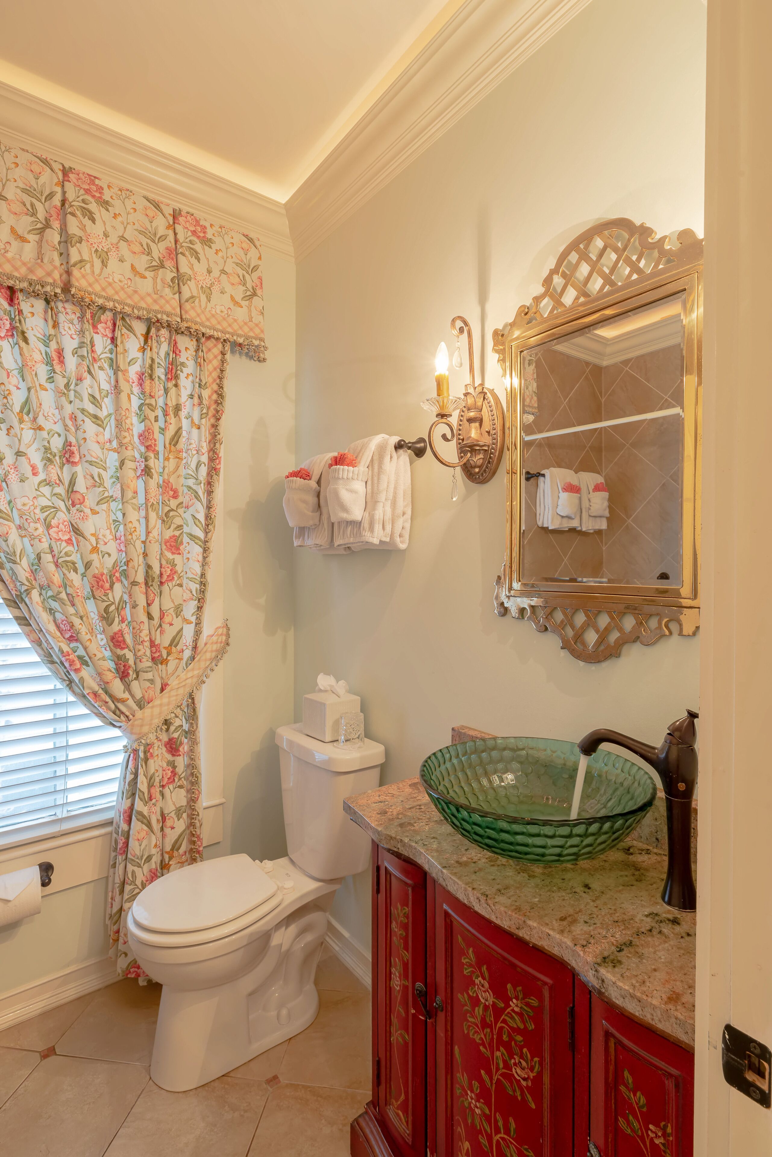 A bathroom with a toilet, a green glass bowl sink, a mirror, and a towel rack.