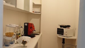 A compact kitchen with white cabinets, a coffee machine, a microwave, and a small dining area with two chairs. - Beauty house (Reggio Calabria)