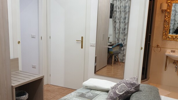 A hotel room with a bed, a small desk, a trash bin, a bathroom with a mirror and sink, and a shower area. - Beauty house (Reggio Calabria)