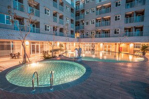 Une cour dotée de deux piscines, d’un espace de détente et d’un bâtiment avec des balcons.