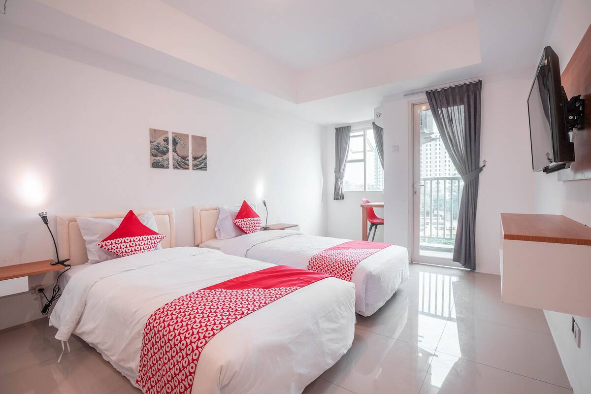 Habitación de hotel con dos camas, un escritorio, un televisor y una ventana con cortinas.