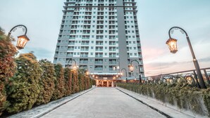 A high-rise hotel with a modern design, featuring a central entrance and a pathway leading to the lobby. - OYO Flagship 728 Baileys Apartment (South Tangerang)