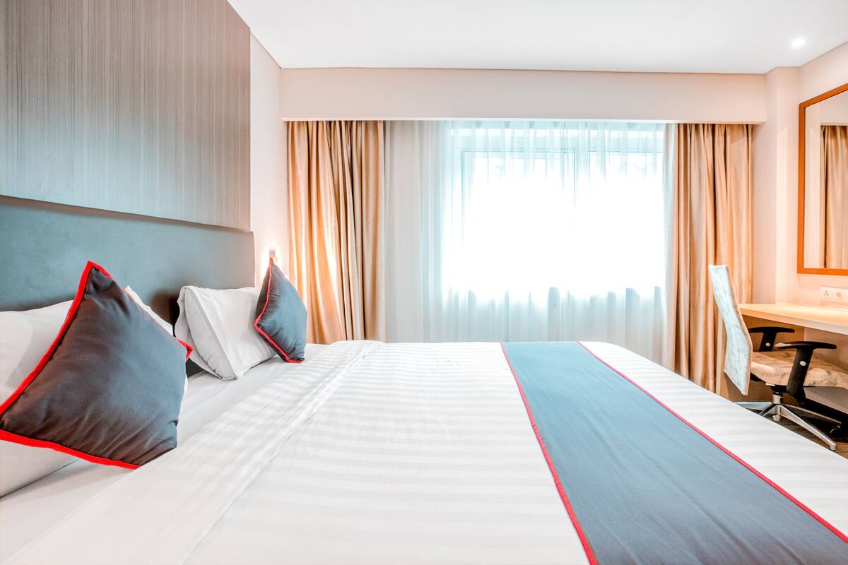 A hotel room with a large bed, a desk, and a chair.
