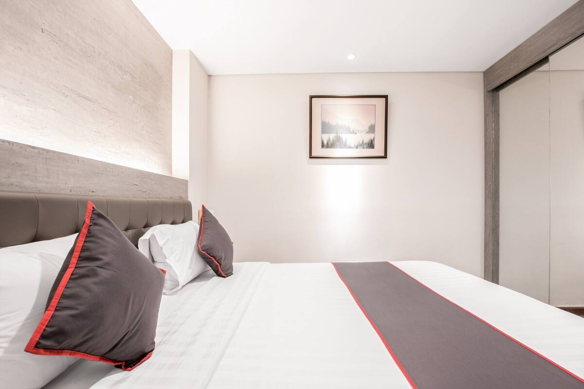 A modern hotel room with a large bed, a headboard, and a framed picture on the wall.