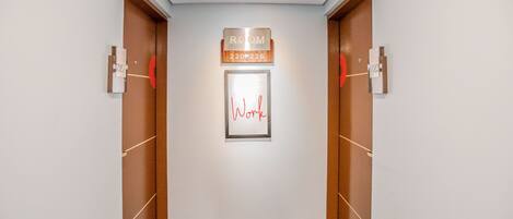 Un pasillo con dos puertas de madera, un letrero que indica 'ROOM 220-226' y una obra de arte enmarcada con la palabra 'Work'.