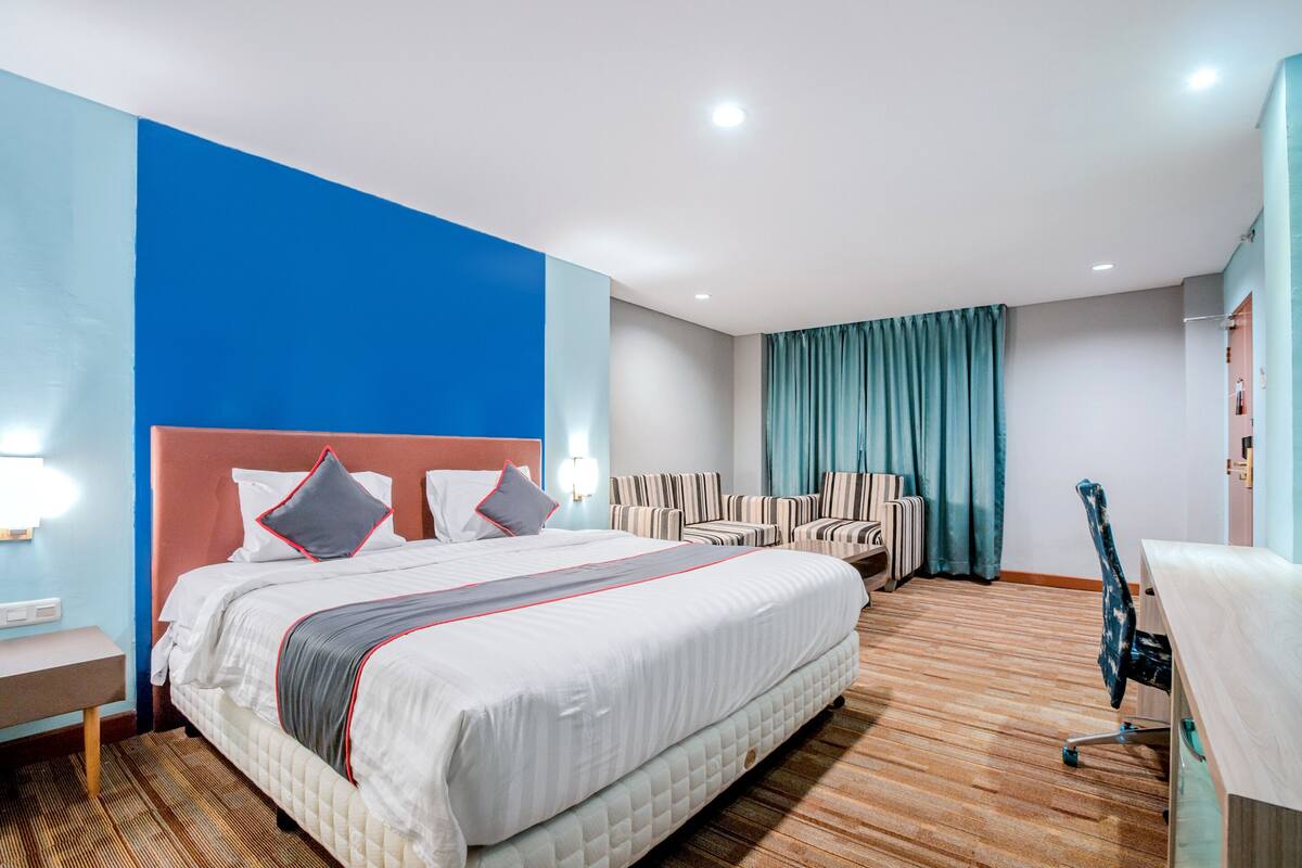 A hotel room with a large bed, a desk, a chair, and a view of the city.