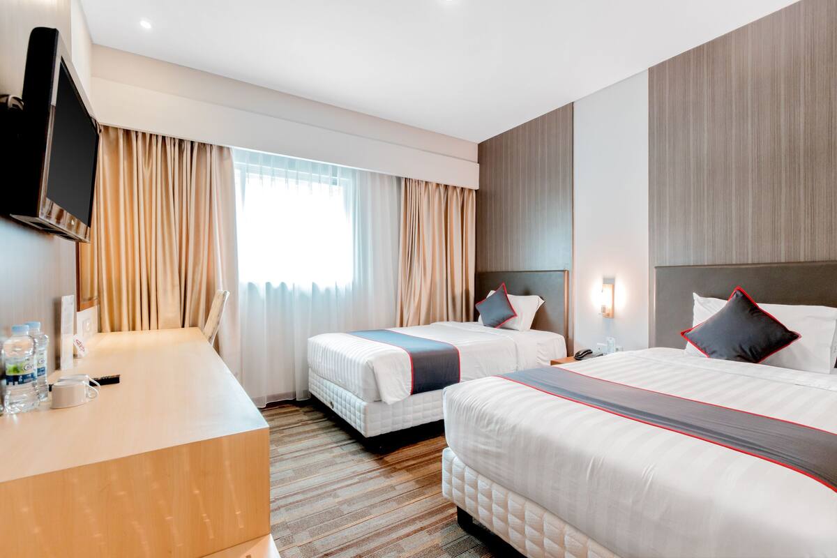A hotel room with two beds, a desk, and a TV.