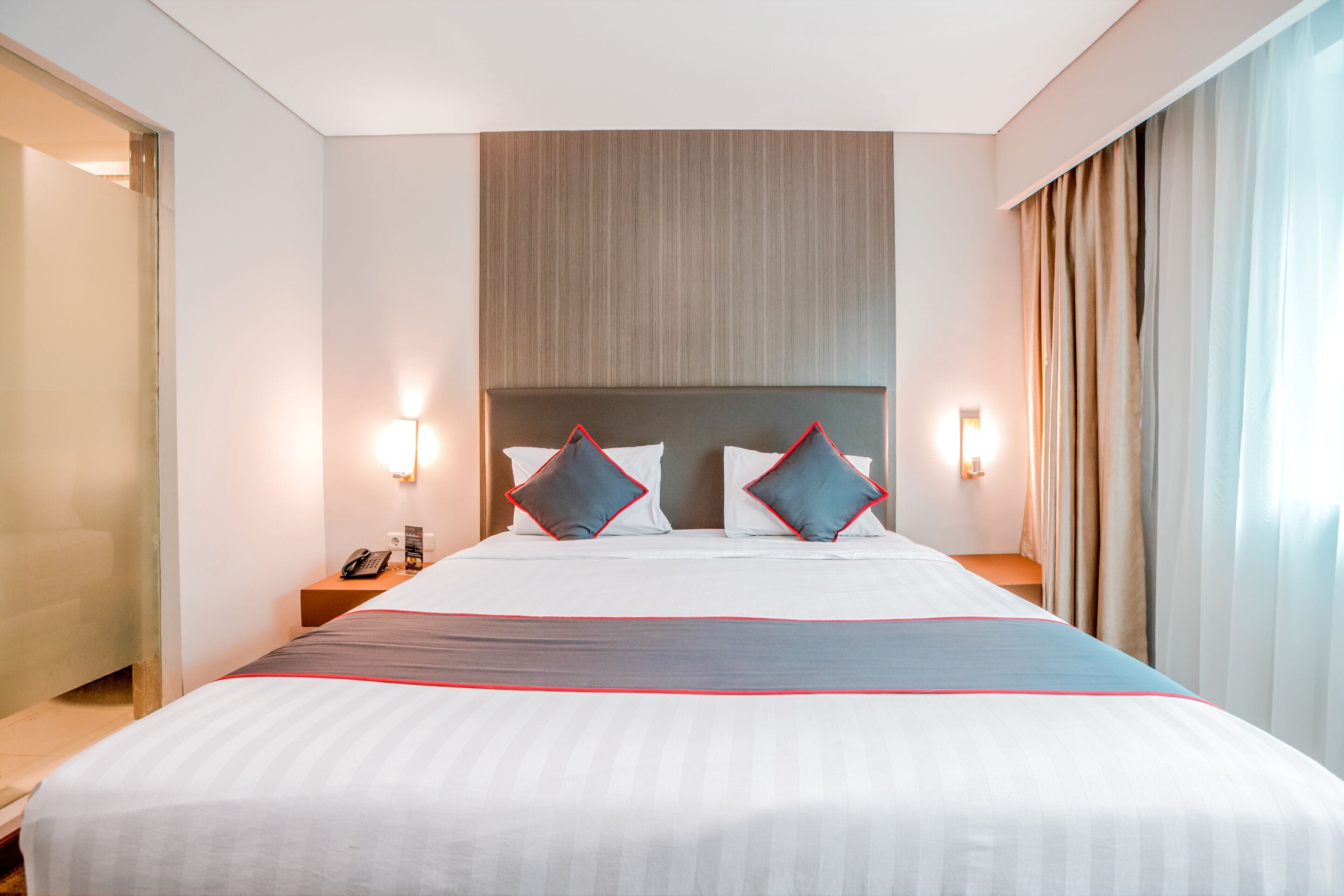 A hotel room with a large bed, two bedside tables, a telephone, and a headboard with a light panel.