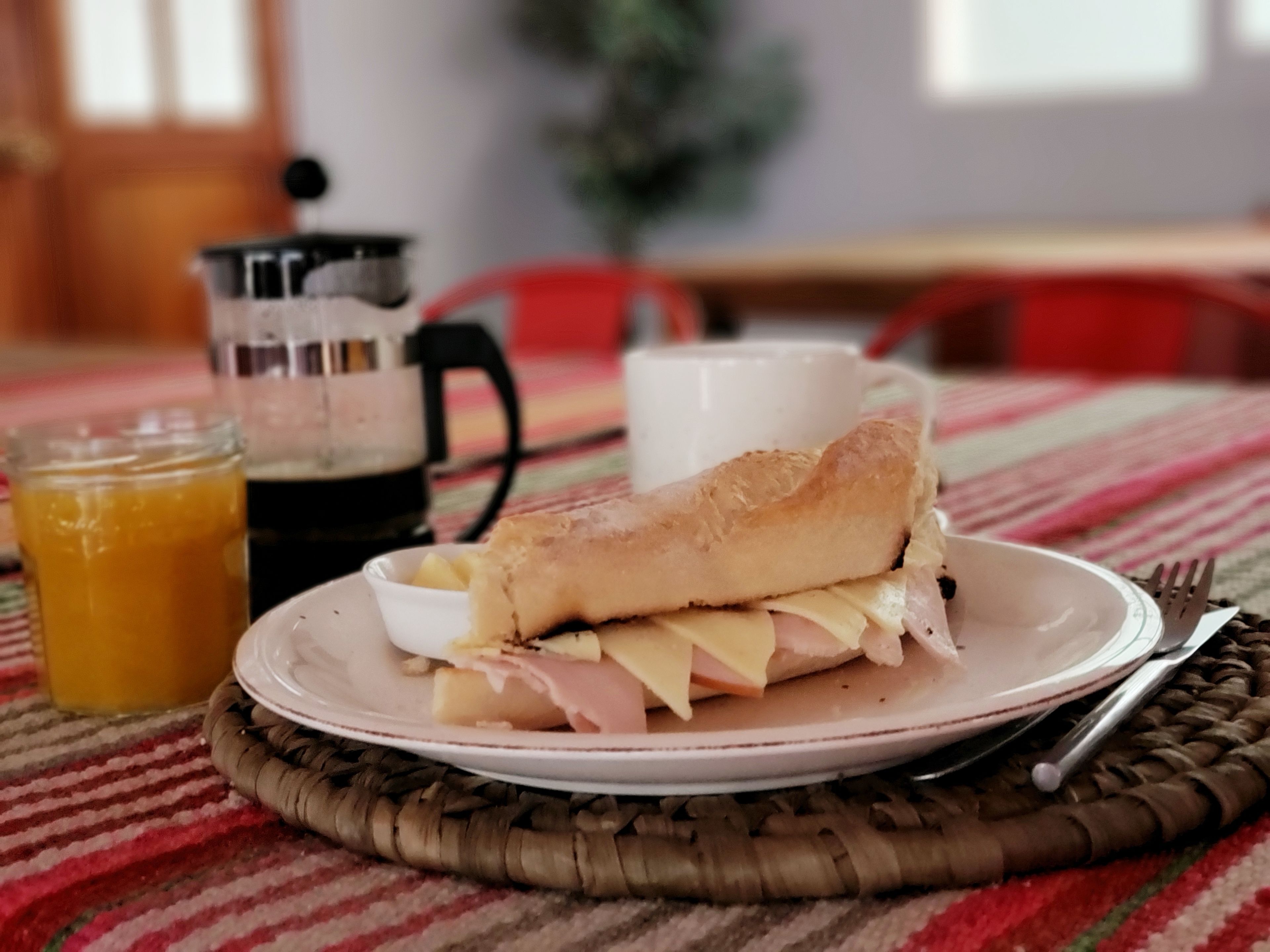 Un sándwich en un plato con una taza y un vaso de jugo sobre una mesa.