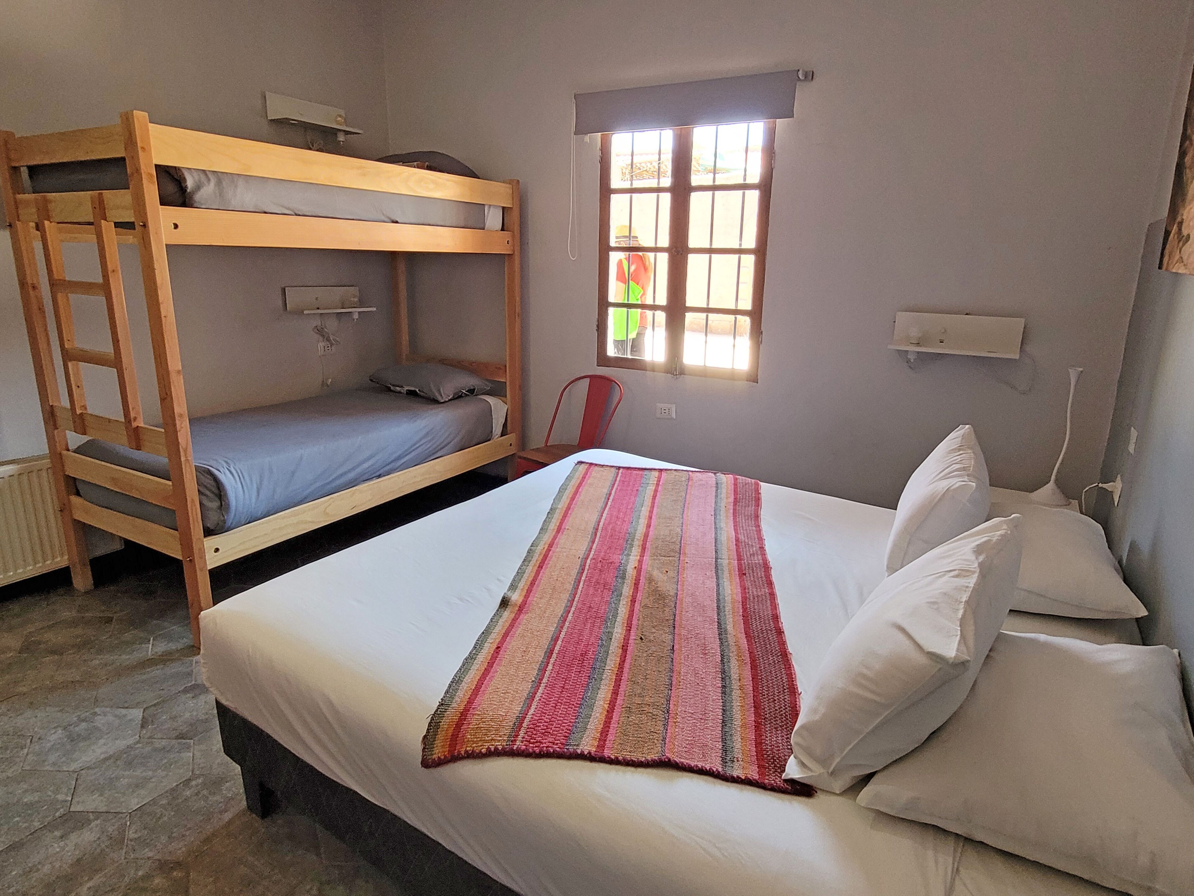 A room with a bunk bed, a single bed, a window with bars, a chair, and a radiator.