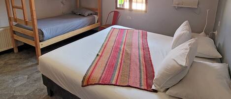 A room with a bunk bed, a single bed, a window with bars, a chair, and a radiator.