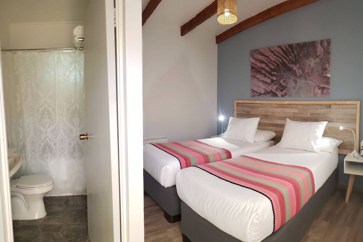 Een slaapkamer met een groot bed, een houten hoofdbord, een nachtkastje met een lamp, en een badkamer met toilet en douchegordijn.