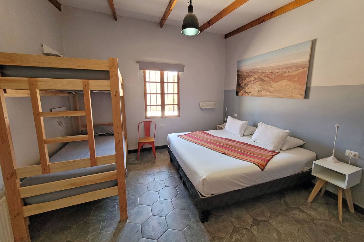 Een slaapkamer met een stapelbed, een eenpersoonsbed, een raam, een schilderij en een nachtkastje.