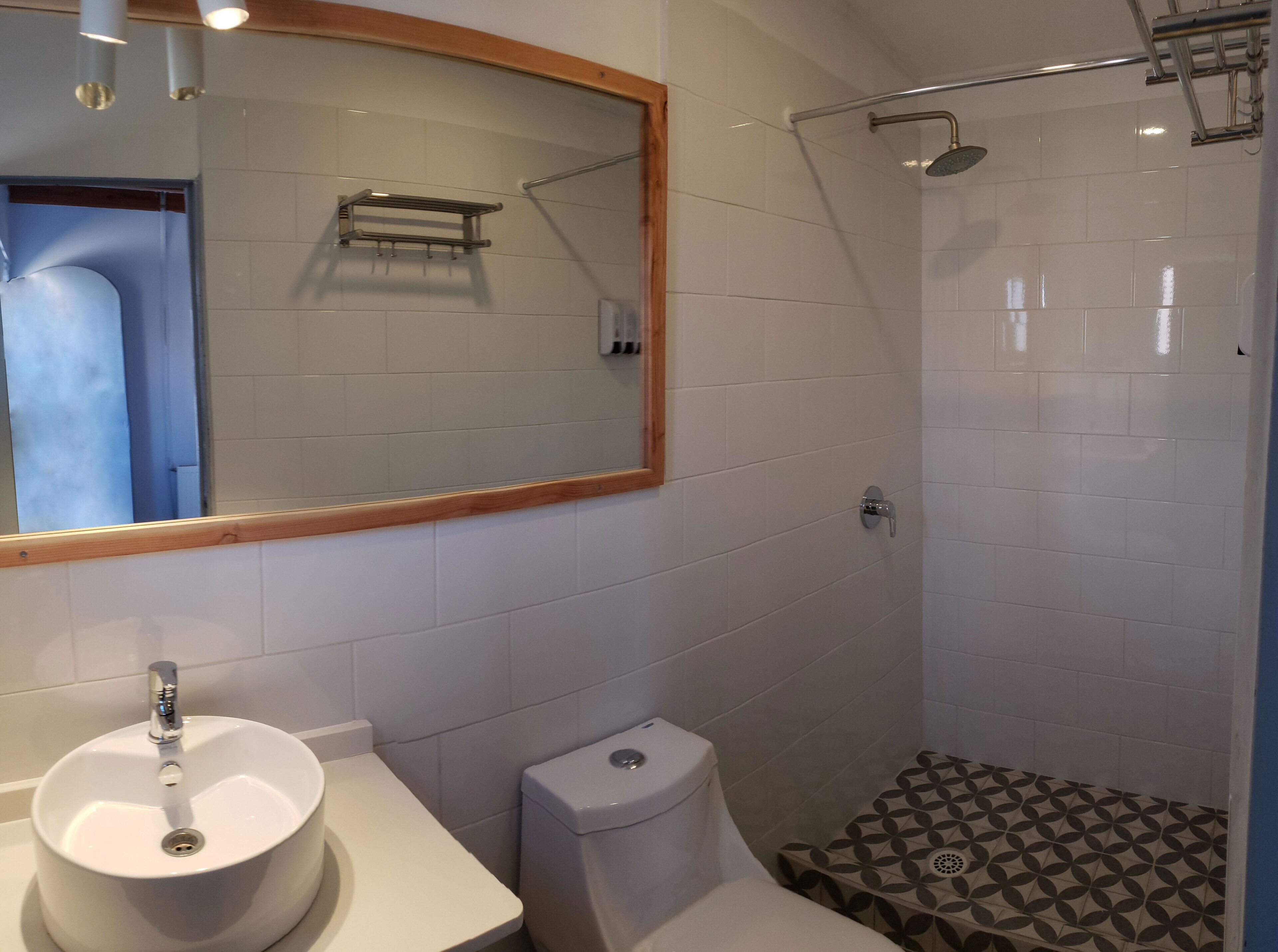 A bathroom with a sink, toilet, shower, and a mirror with a wooden frame.