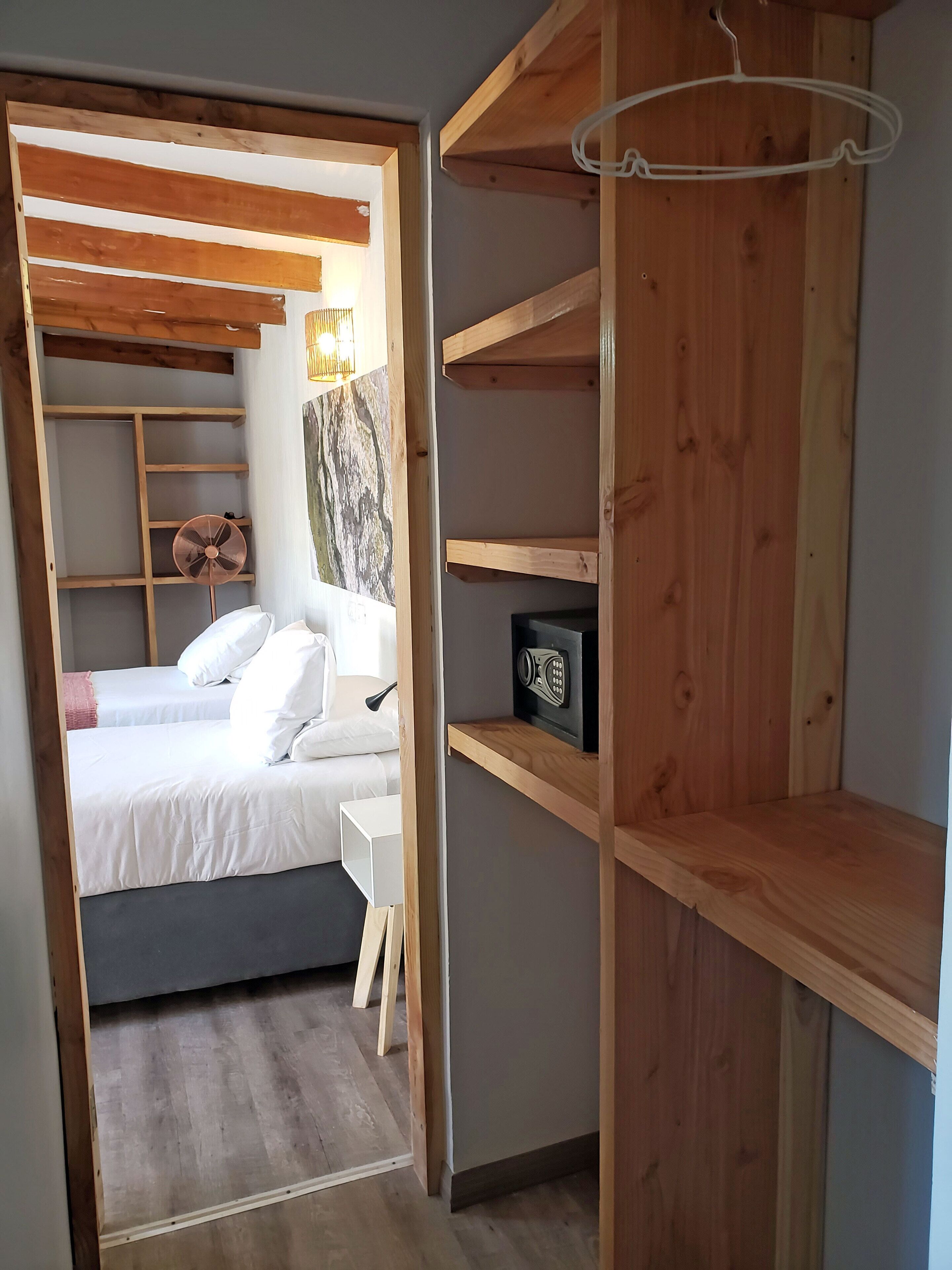A bedroom with a bed, bedside tables, a fan, and a wooden wardrobe with shelves.