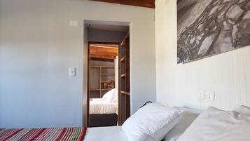 A bedroom with a bed, a striped blanket, a wooden ceiling, a wardrobe, and a painting on the wall.