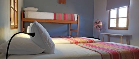 Un dormitorio con dos camas, un ventilador de pie, una ventana y vigas de madera en el techo.