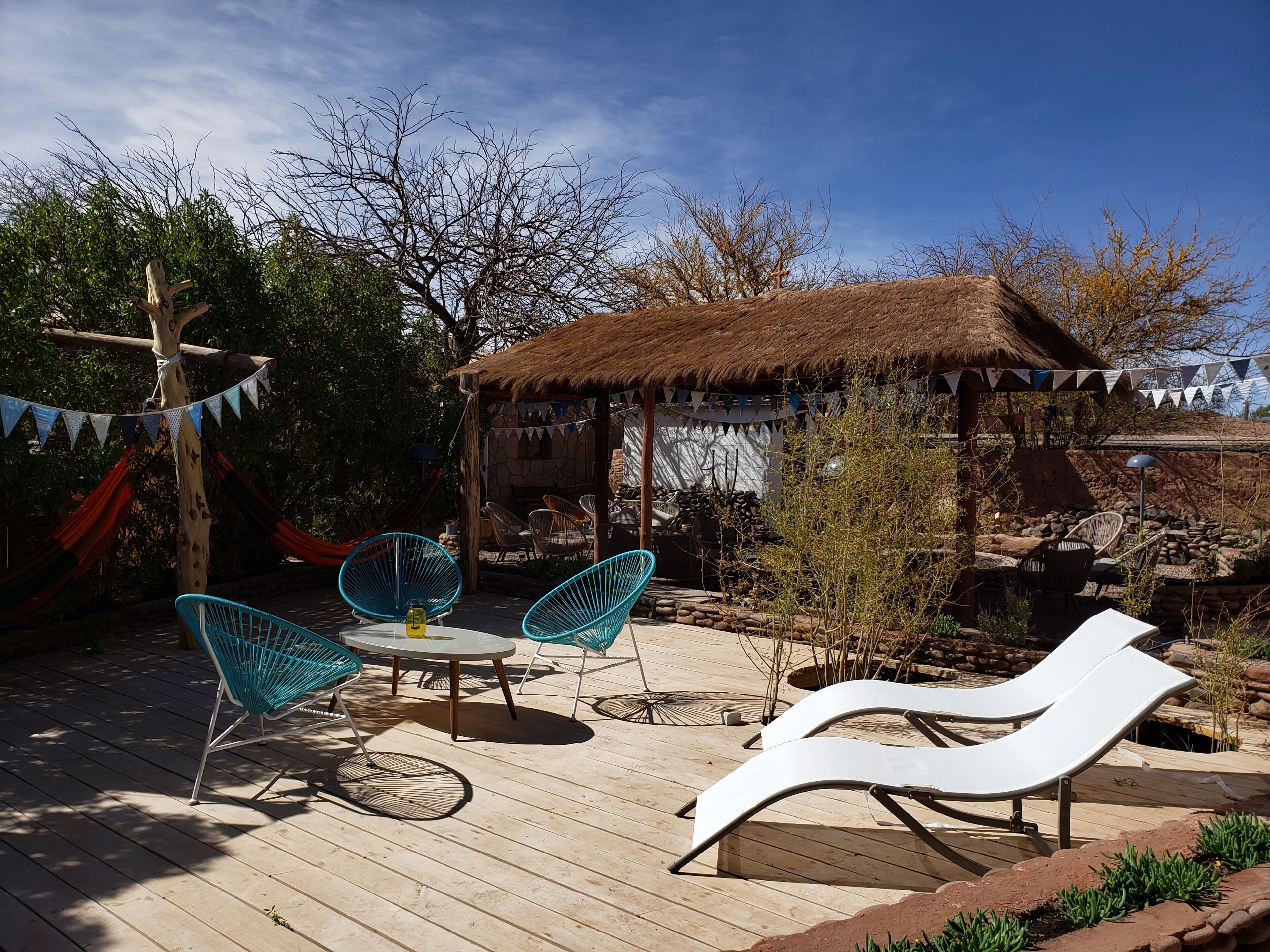 Eine Holzterrasse mit Liegestühlen, einem Tisch und einer Struktur mit einem Reetdach.