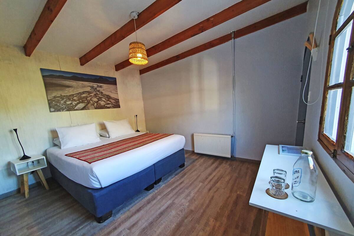 Een slaapkamer met een bed, bureau, radiator en raam.