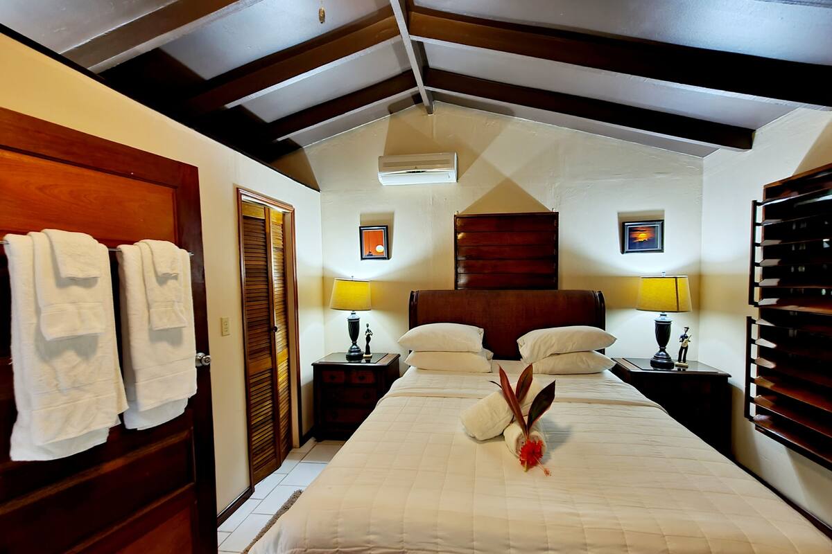Une chambre d’hôtel avec un grand lit, une tête de lit en bois, deux tables de chevet avec des lampes, une armoire en bois et deux serviettes accrochées au mur.