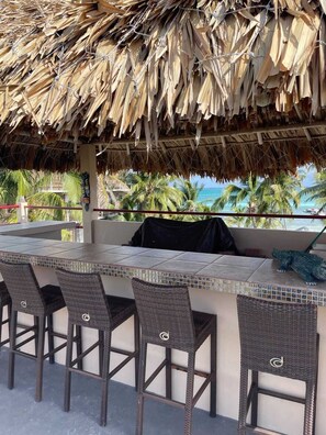 An outdoor seating area with a thatched roof, wicker chairs, and a view of the ocean. - Yocamatsu (Caye Caulker)