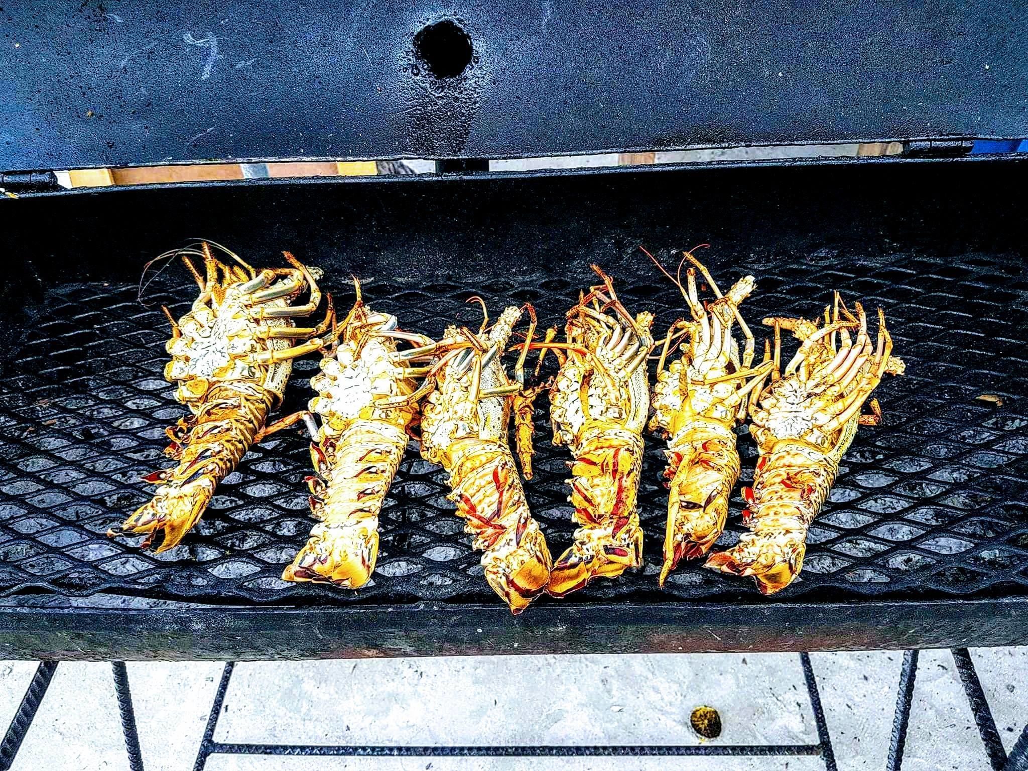 Lobsters being grilled on a black grill with a textured surface.