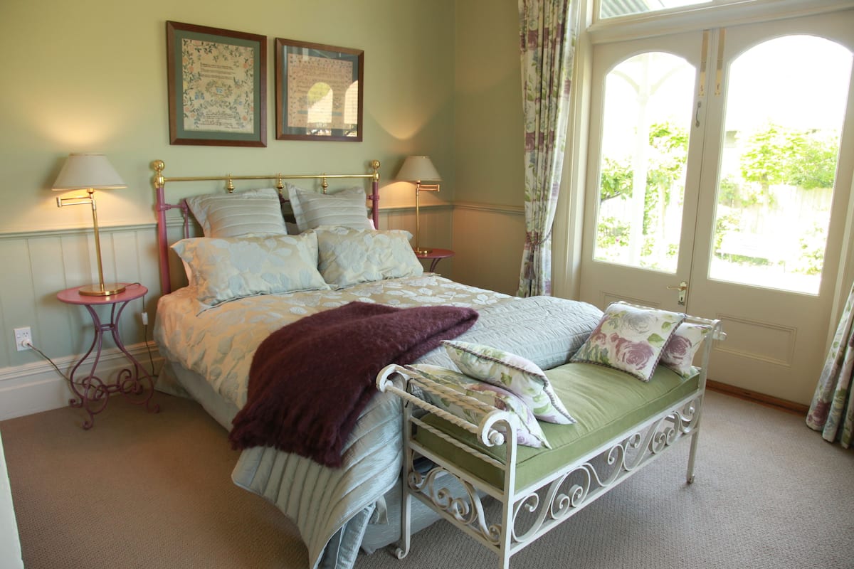 Une chambre à coucher comprenant un lit, deux tables de chevet, une fenêtre avec des rideaux et deux tableaux accrochés au mur.
