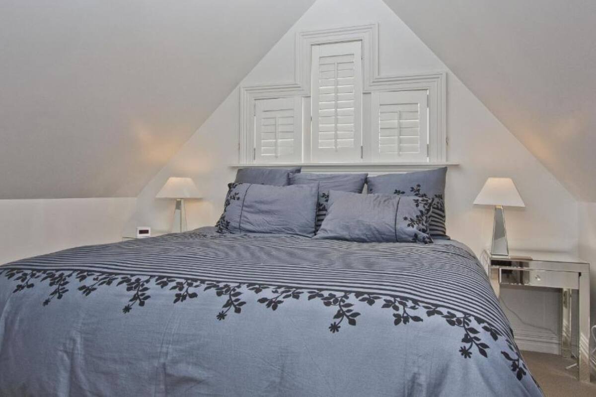 Une chambre à coucher comprenant un lit, deux tables de chevet, un bureau et une fenêtre avec des volets.