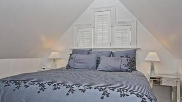 A bedroom with a bed, two bedside tables, a desk, and a window with shutters.