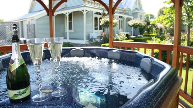 Een hottub met champagneglazen en een fles op een houten terras.