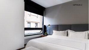 Ett modernt hotellrum med en stor säng, ett nattduksbord, en lampa och utsikt över staden genom ett fönster.
