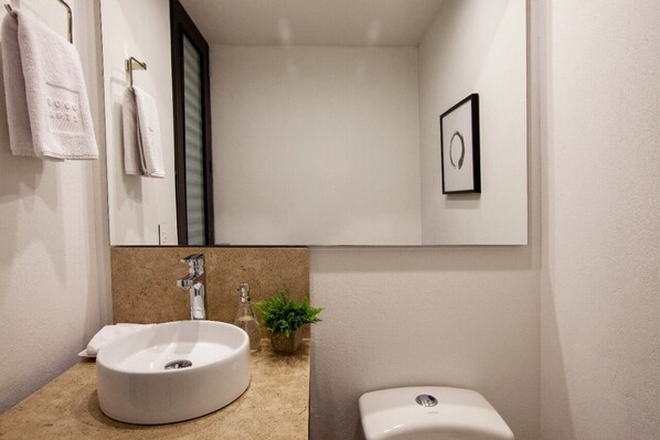 A modern bathroom with a white sink, a toilet, a mirror, and a framed picture on the wall.
