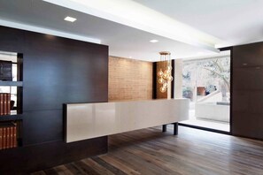 A modern reception area with a wooden panel wall, a white reception desk, and a hanging light fixture. - Stunning Executive Apartment with High Cleaning Standards (Bogotá)