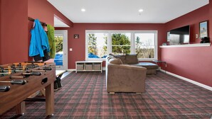 Una habitación con mesa de futbolín, sofá y televisor en la pared.