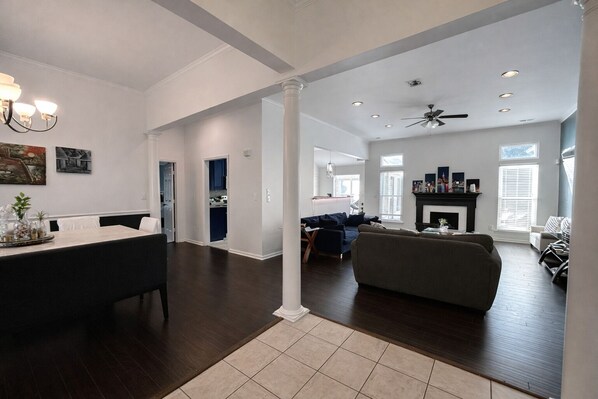 A spacious living area with a dark wood floor, a gray sofa, and a dining area with a long table and chairs.
