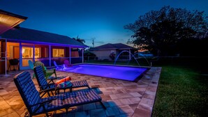 Un patio exterior con piscina, sillas de descanso y una zona cubierta con una parrilla.