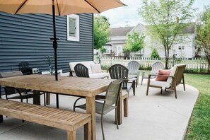 Een terras met een houten tafel en stoelen, een parasol en uitzicht op een wijk.