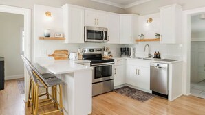 A modern kitchen with white cabinets, stainless steel appliances, and a bar stool area. - Remodeled Home Near Beach and Downtown (Manistee)