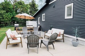 Een terras buiten met een eettafel, stoelen en een grote parasol.