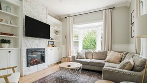 A living room with a fireplace, a sofa, a coffee table, and a TV mounted on the wall. - Remodeled Home Near Beach and Downtown (Manistee)