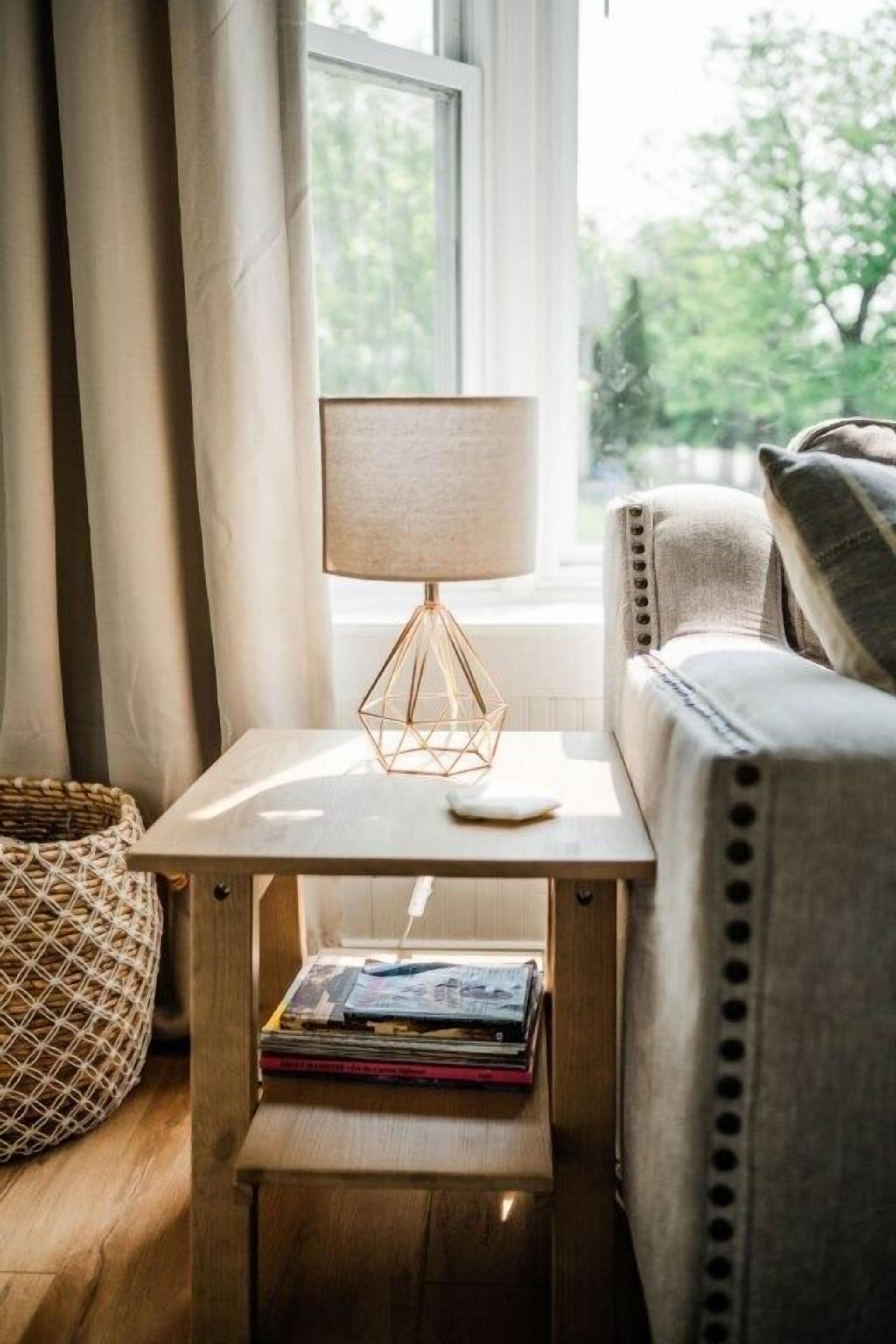 Una habitación acogedora con una mesita de noche de madera, una lámpara y una pila de libros.