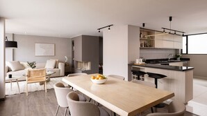 A modern kitchen with a central island, a dining area with a wooden table and chairs, and a living area with a sofa and a coffee table. - NEW DESIGN DUPLEX - BOGO64 303 (Bogotá)