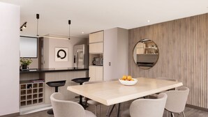 A modern kitchen with a central island, a dining area with a light-colored table and matching chairs, and a wooden accent wall with a mirror. - NEW DESIGN DUPLEX - BOGO64 303 (Bogotá)