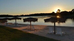 A beach with lounge chairs and thatched umbrellas, a calm lake, and a sunset in the background. - Meadows - Townhome in Bernard`s Landing with all the amenities to enjoy! (Moneta)