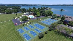 An aerial view of a property with multiple tennis courts, a swimming pool, and a large body of water in the background. - Meadows - Townhome in Bernard`s Landing with all the amenities to enjoy! (Moneta)