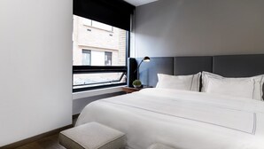 Une chambre d’hôtel moderne avec un grand lit, une table de chevet, une lampe et une vue sur la ville par la fenêtre.