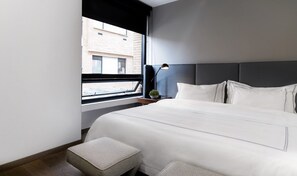 Une chambre d’hôtel moderne avec un grand lit, une table de chevet, une lampe et une vue sur la ville par la fenêtre.
