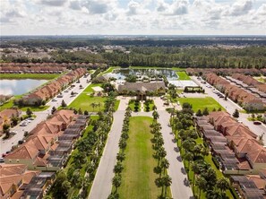 Stroll through a serene park with a tranquil pond surrounded by manicured lawns and a variety of trees.