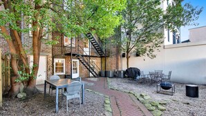 Ein Terrassenbereich im Freien mit einem gepflasterten Weg, Sitzgelegenheiten und einem Feuerkorb.